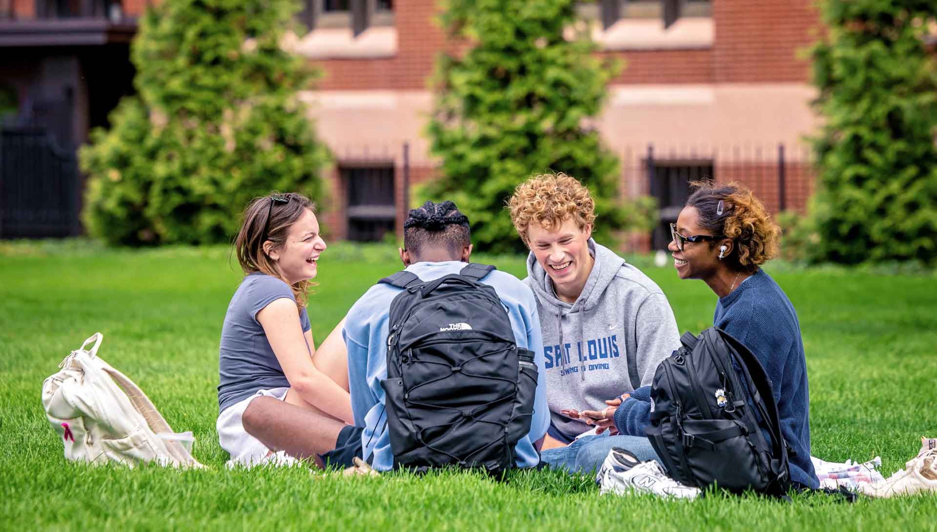 Four students laughing together on a campus grassy area