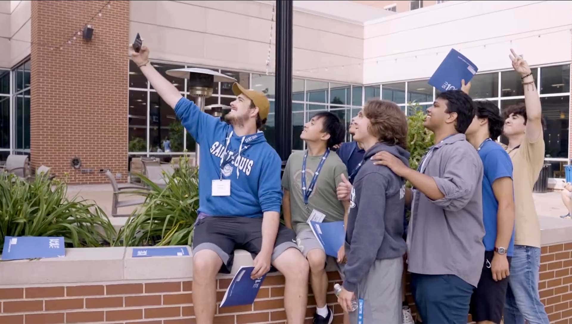 A group of male students smile and pose for a selfie outside of SLU’s Grand Hall.