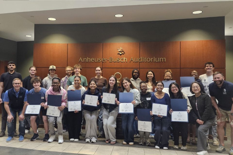 Leadership Academy 2026 a large group of people stand posed holding certificates in front of the Anheuser Busch Auditorium