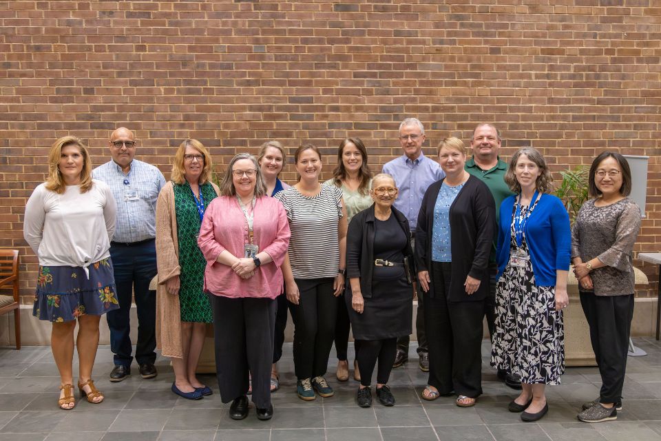 Libraries Cohort 2025 group of people smiling and posing in front of a brick wall
