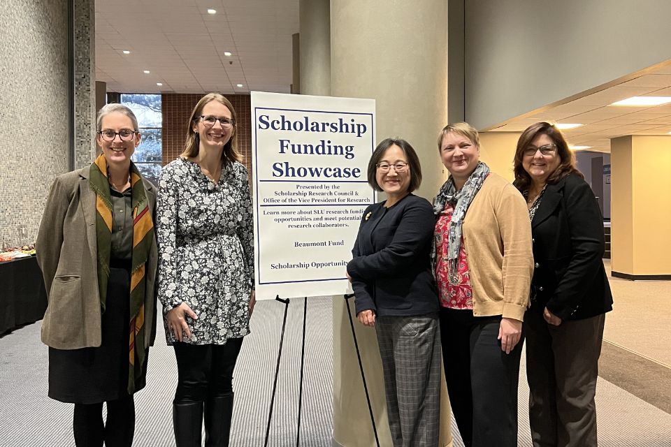 OVPR Scholarship Showcase 2025 five women standing smiling and posed with a sign reading scholarship funding showcase sign
