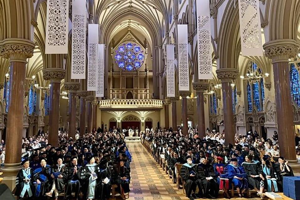Interior of a church with the pews full of graduates, professors and families