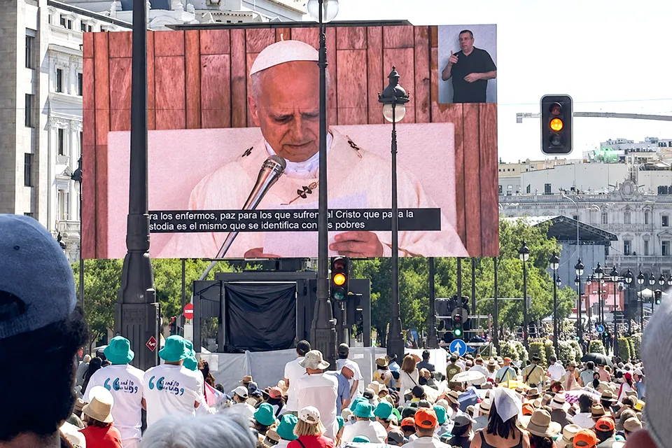 A large crowd of faithful fills the streets of downtown Madrid during the Pope's visit as they watch a large screen showing his image.