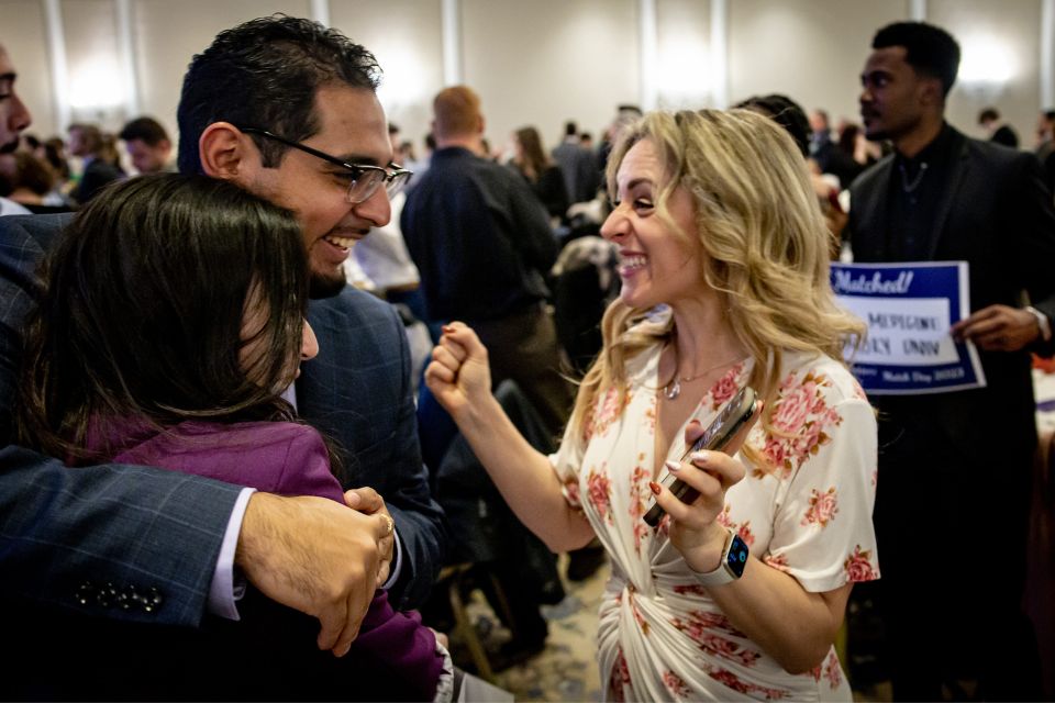 Two people hug next to a woman smiling excidely during a Match Day event.
