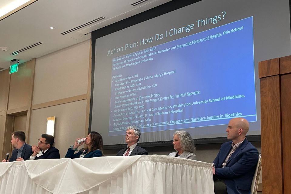 Five panelists seated in front of a projection screen during a medical business ethics summit.
