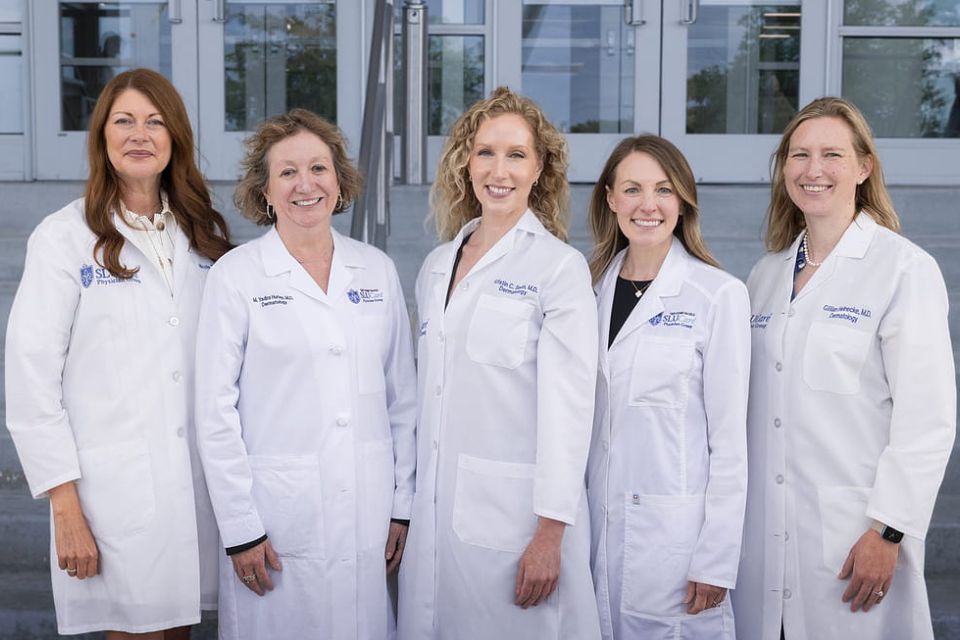 Five faculty members of the dermatopathology program stand in front of a building