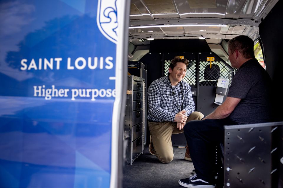 A physicians kneels next to a patient sitting inside a mobile health clinic.