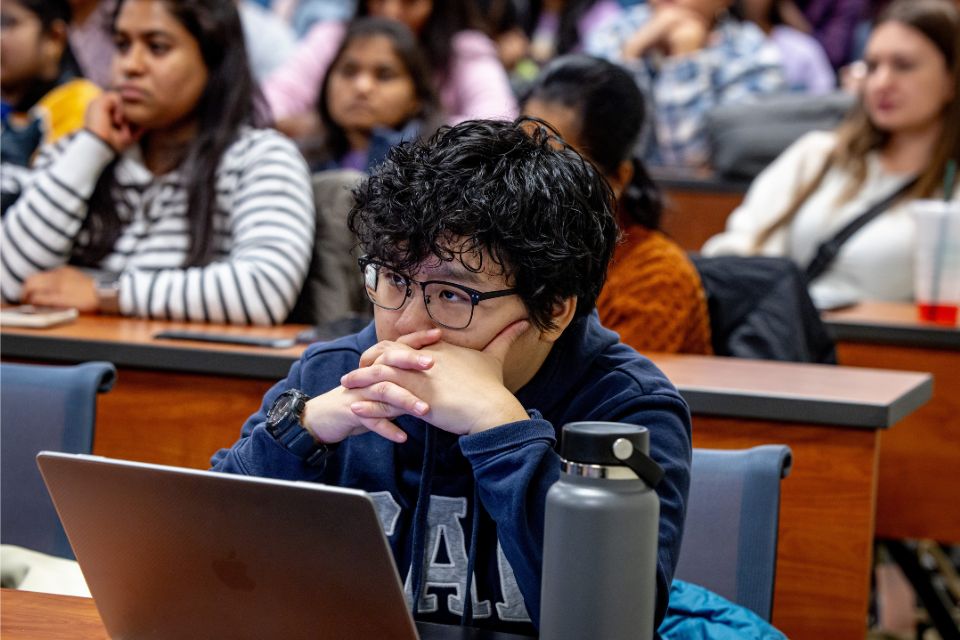 Student sits in front of laptop inside a lecture hall.