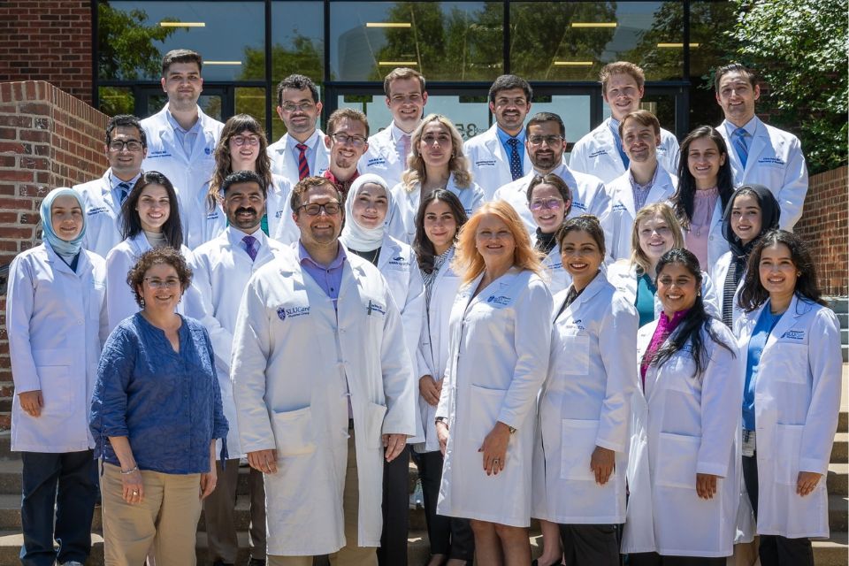 A group shot of neurology residents in white coats standing in front of a brick building entrance.