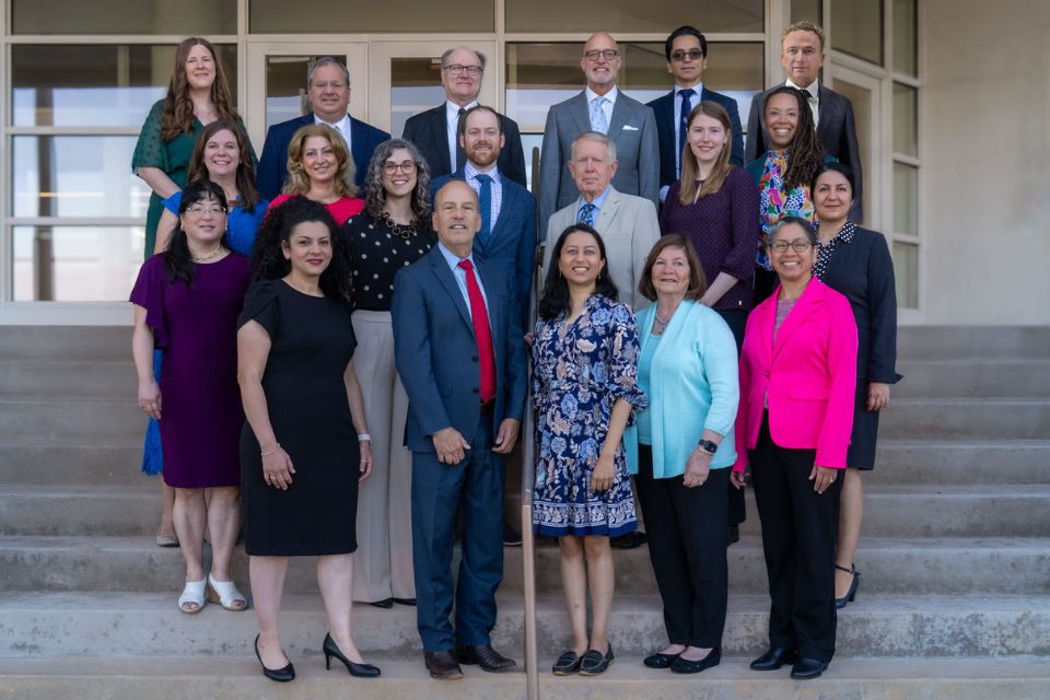 A group shot of professionally dressed individuals posing on the front steps of an office building.