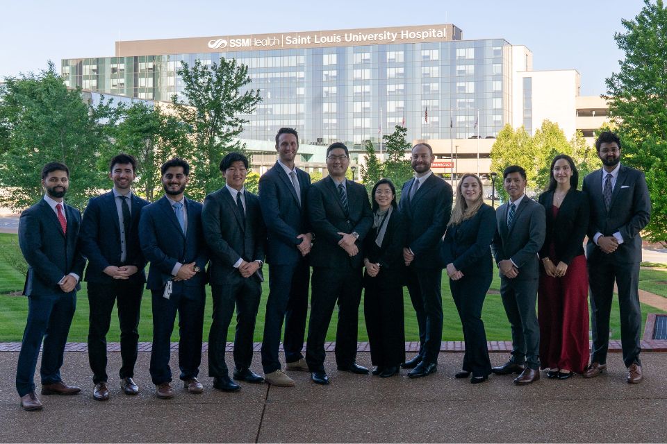 Ophthalmology residents A group shot of inividuals dressed in formal attire posing outdoors with SSM Health Saint Louis University Hospital in the distance.