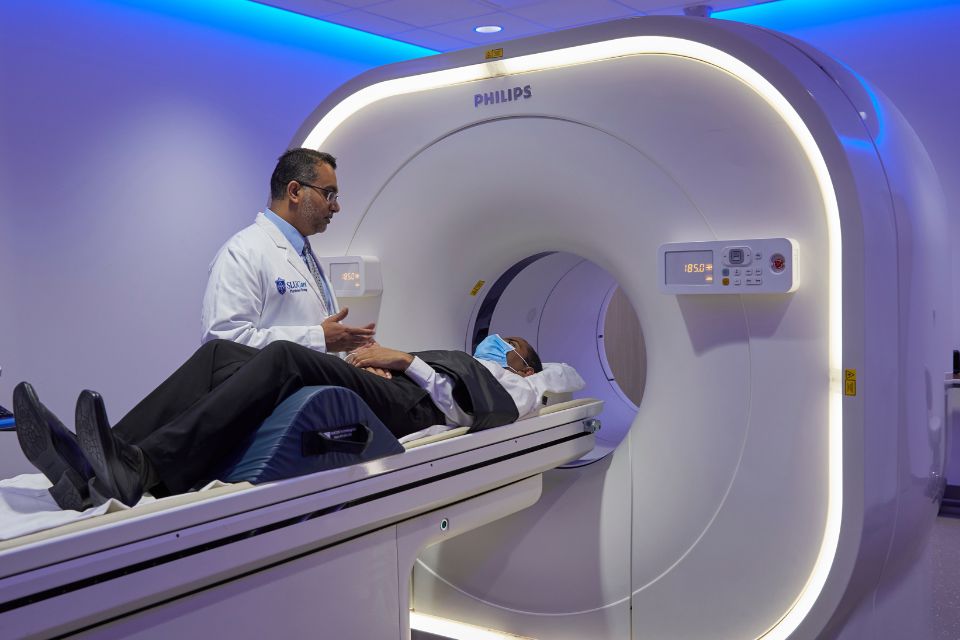 A doctors assists a patient as they enter a large, tube-shaped imaging machine for a scan.