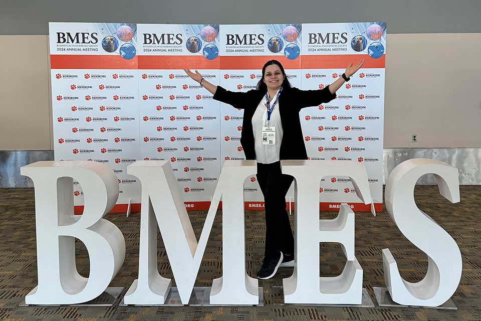 Student Travel Award A student researcher stands in front of giant letters that read BMES.